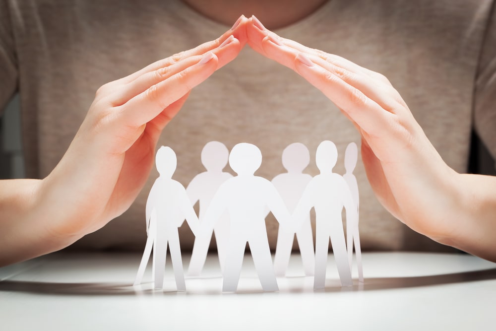 Des mains protégeant des silhouettes humaines, symbole de solidarité et de protection sociale